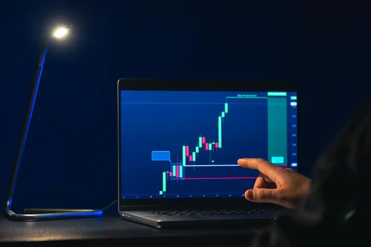 Trading chart on a laptop with a hand pointing at the setup